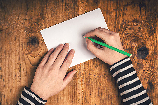 Woman writing recipient address on mailing envelope, female hands from above on office desk sending letter, top view, retro toned.